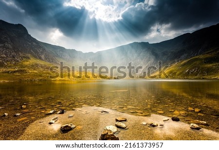 The sun breaks through the clouds over a mountain lake. Sun breaking through clouds over mountain lake landscape. Mountain lake landscape. Lake in mountains Royalty-Free Stock Photo #2161373957