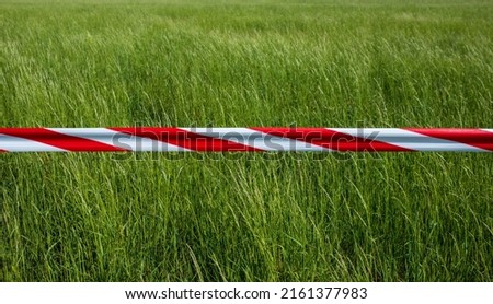Red and white barrier tape as a boundary in front of a meadow to protect breeding birds. 