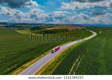 red truck driving on asphalt road along the green fields. beautiful clouds in the sky. Aerial view landscape. drone photography. cargo delivery and transportation concept.
