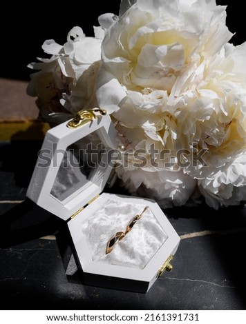 Wedding rings in an open white box with a wedding bouquet of white peonies lie on the stairs with sunlight