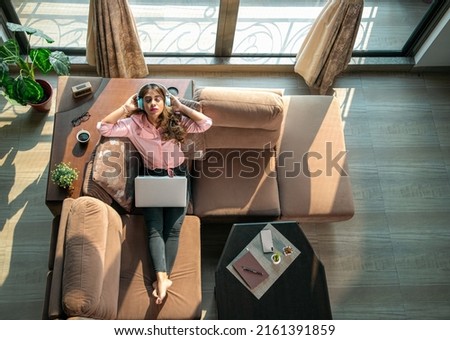 A young modern attractive and beautiful Asian Indian female or woman is taking a break from work and absorbed in listening to music on headphones with eyes closed in an apartment or interior house. Royalty-Free Stock Photo #2161391859