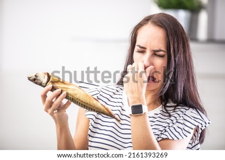 Woman holds stinky fish holds her nose with disgusted facial expression from the smell. Royalty-Free Stock Photo #2161393269