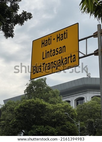 Steet sign saying “Warning, Transjakarta bus track.” Transjakarta is a bus rapid transit (BRT) system in Jakarta, Indonesia. Royalty-Free Stock Photo #2161394983