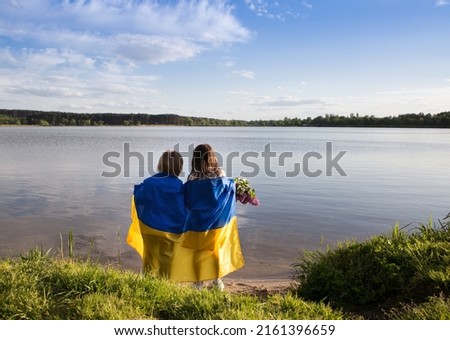 children stand with their backs on the shore of a lake with a blue-yellow Ukrainian flag. Family, refugees, unity, support. Ukrainians are against the war. stand with Ukraine