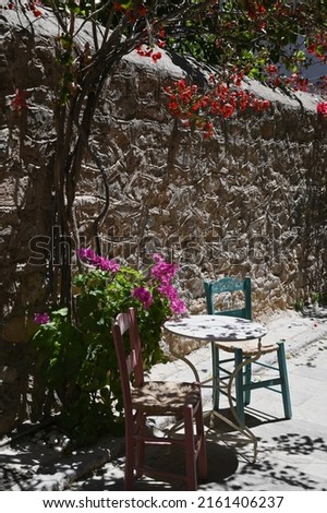 Traditional rural house patio with a bistro table and wooden wicker chairs against a textured wall in Nafplio, Greece. 