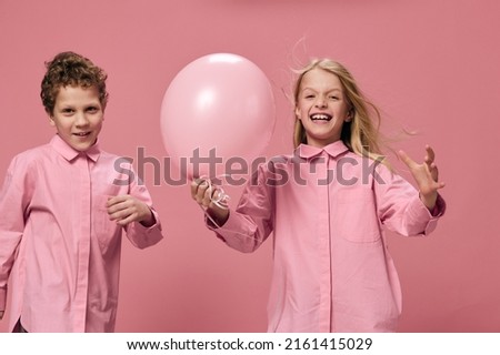 cute happy kids in pink clothes on a pink background have fun playing with colored balloons enjoying childhood