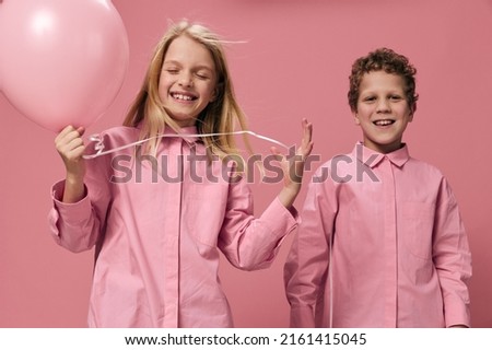 beautiful joyful children brother and sister stand on a pink background in pink clothes with a pink balloon in their hand and the girl closed her eyes from enjoyment
