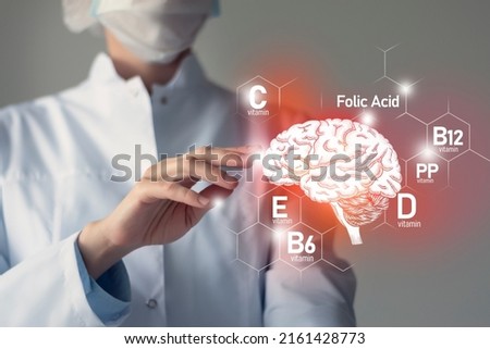 Essential nutrients for Brain health including vitamin C, vitamin B, folic acid, vitamin PP. Blurred portrait of doctor holding highlighted Brain. Royalty-Free Stock Photo #2161428773