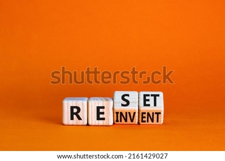 Reinvent and reset symbol. Turned wooden cubes and changed the concept word Reinvent to Reset. Beautiful orange table orange background. Business reinvent and reset concept. Copy space.