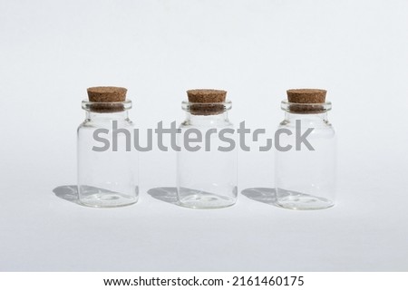 Three small glass jars with a cork for cosmetics or aroma oils on a white background