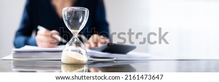 Businesswoman calculating bill behind sand running through the bulbs of an hourglass
