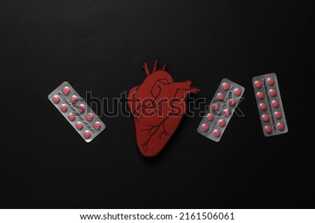 Treatment of cardiovascular disease concept. Paper cut anatomical heart with stethoscope and pills on black background. Top view