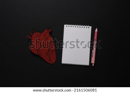 Diagnosis of heart disease. Anatomical heart with notebook on black background