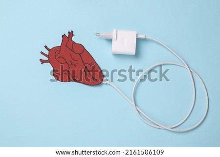 Charge your heart. Anatomical heart with charger cable on a blue background. Energy charge.