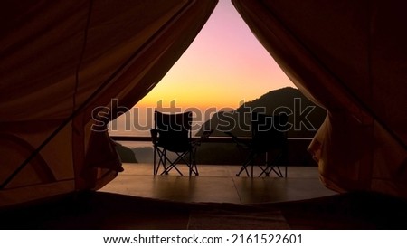 Tourist tent in camp among with mountain view on sunrise. View from tent camping on amazing sunrise with mountains and two folding camping chair. Travel vacation on nature Royalty-Free Stock Photo #2161522601