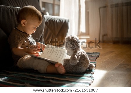 a boy with a bear looks at pictures in a book