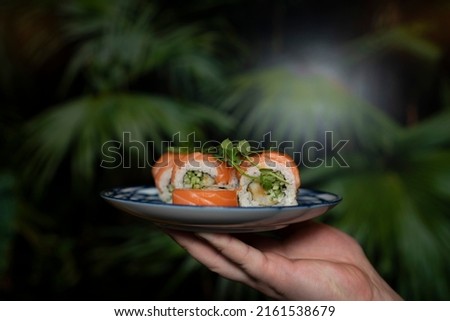 Sushi with salmon, cucumbers, shrimp, microgreens on plate in hand