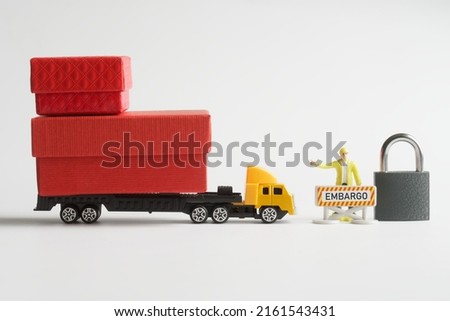 Toy truck with trailer loaded with boxes of goods is stopped next to a prohibition road sign, customs officer and padlock. Сoncept of trade sanctions and blocking the delivery of goods. Close-up