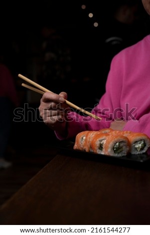 Girl in pink sweater eat sushi with salmon, cucumbers, shrimp, microgreens. 