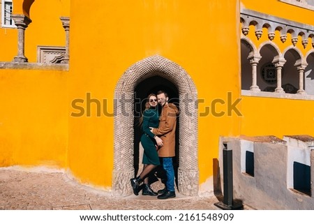 A loving couple stands in the arch of the yellow wall of the beautiful Pena Palace in Portugal