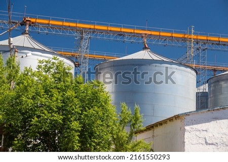 Granary elevator, Ukrainian grain storage on blue sky and green trees background. International wheat, seed and corn supplier. War 2022 in Ukraine Royalty-Free Stock Photo #2161550293