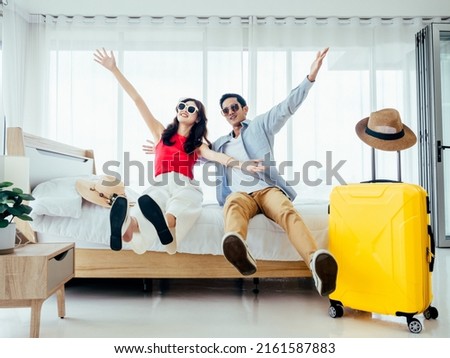 Ready to travel, happy holiday, check-in. Summer vacation concept. Asian couple raising hands with joy, man and woman wear sunglasses smile with happy on white bed with yellow suitcases on a trip. Royalty-Free Stock Photo #2161587883