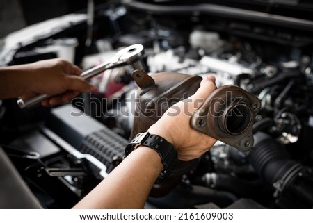 Close up old catalytic converter in hand Car service man and holding a wrench for remove part in engine room of car , service and maintenance concept in garage Royalty-Free Stock Photo #2161609003