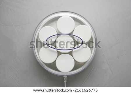 Modern yogurt maker with jars on light grey table, top view