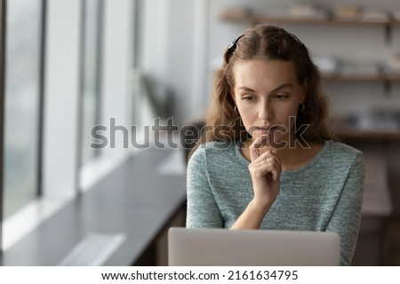 Thoughtful serious gen Z student girl using laptop at home. Young employee, female entrepreneur looking at monitor with pensive face, thinking over work on project, reading email, chatting online Royalty-Free Stock Photo #2161634795