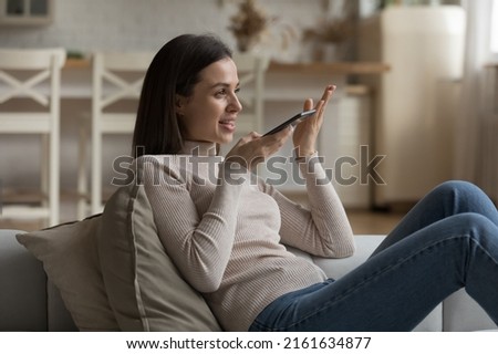 Happy engaged millennial girl using Internet app, voice virtual assistant on smartphone, recording audio message, talking on mobile phone, making call on speaker. Wireless communication concept Royalty-Free Stock Photo #2161634877