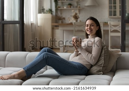 Cheerful beautiful girl drinking hot tea, cocoa, chocolate, holding cup, mug, enjoying morning coffee, leisure, relaxing at home, looking at camera, smiling. Indoor portrait