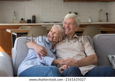 Healthy happy old couple pensioners cuddle on sofa look at distance dream spend good days together on retirement. Loving affectionate mature husband wife rest on couch imagine visualize future plans Royalty-Free Stock Photo #2161635027