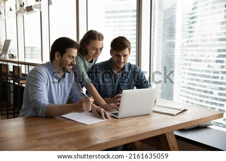 Creative business team sharing laptop in office, watching startup presentation, design project, discussing ideas, brainstorming, pointing at monitor, talking. Office employees meeting at computer Royalty-Free Stock Photo #2161635059
