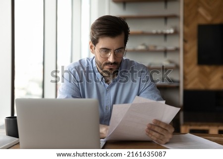 Focused businessman reviewing paper reports, received letter, notice from bank, working at office workplace with laptop. Legal expert, professional, lawyer reading, checking financial documents Royalty-Free Stock Photo #2161635087
