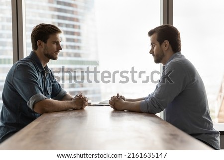 Two businessmen competing for leadership, meeting in office, sitting opposite at table with clasped hands in silence. Business partners arguing, having difficult negotiations, problem in relationships Royalty-Free Stock Photo #2161635147