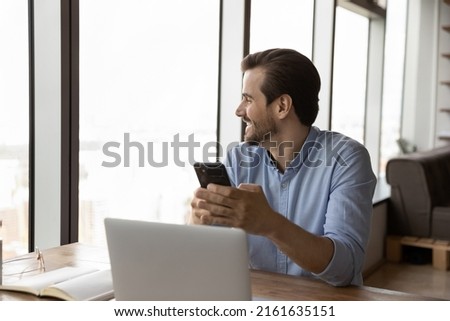 Happy businessman thinking over telephone call, getting good news from text message, looking out of window, pondering on business project future vision. Thoughtful smartphone user chatting online