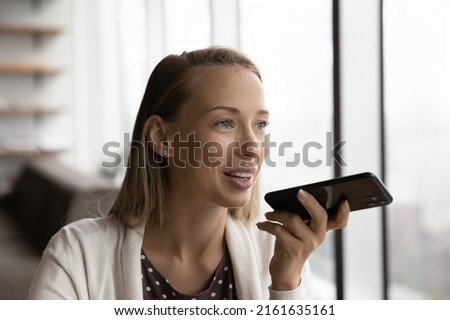 Happy thoughtful smartphone user recording audio message. Young blonde woman, office worker, businesswoman using voice recognition app, giving command to virtual assistant, chatting on messenger