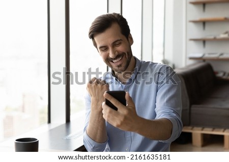 Happy excited businessman looking at smartphone screen, making winner yes gesture, smiling and laughing. Satisfied millennial man using mobile phone, reading good news, celebrating achieve, success Royalty-Free Stock Photo #2161635181