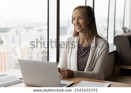 Happy distance employee in headphones using laptop for video call and virtual conference meeting, looking away, thinking of conversation. Student attending remote class, online training Royalty-Free Stock Photo #2161635191