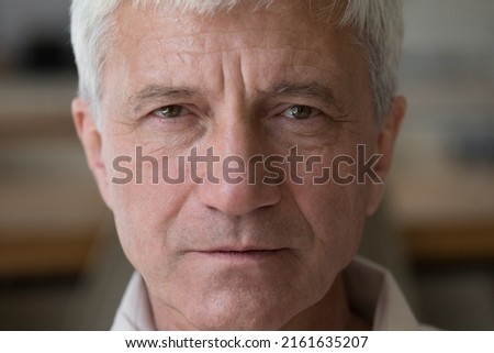 Close up portrait wrinkled face hoary senior man grandfather retiree posing indoors with unhappy serious look. Thoughtful grey haired old male pensioner stand at home look at camera ponder on problems Royalty-Free Stock Photo #2161635207