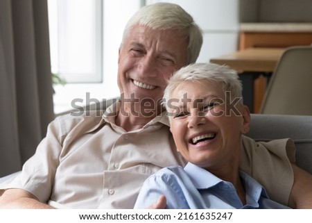 Laughing older age married couple embrace on cozy sofa at living room having fun at home spend happy time on retirement. Smiling elderly spouses having good healthy teeth enjoy sweet moment together Royalty-Free Stock Photo #2161635247