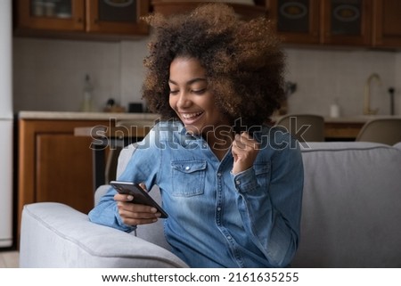 Excited cheerful gen Z African teenager girl using mobile phone, getting surprising good news, looking at screen, laughing, celebrating win, success, luck, achieve, good result Royalty-Free Stock Photo #2161635255