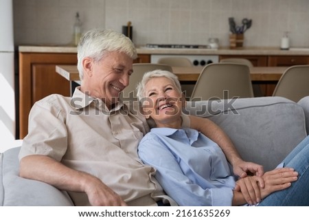Love has no age. Laughing carefree hoary elderly spouses husband wife cuddle on comfy couch talk enjoy romantic moment of bonding. Happy old age family couple spend time together at cozy studio flat Royalty-Free Stock Photo #2161635269