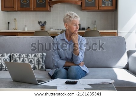 Confused old lady retiree sit on sofa with sad upset look distracted from financial papers debts unpaid taxes think what to do. Distressed worried senior female having no money to pay overdue bills Royalty-Free Stock Photo #2161635341