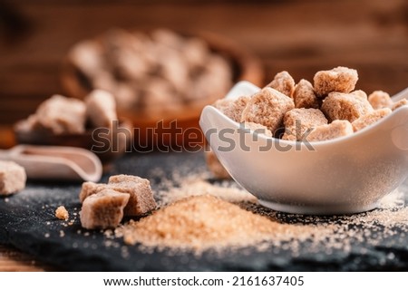 Bowl and scoop with sand and lump brown sugar on wooden background. brown sugar cube. Make unhealthy nutrition, obesity, diabetes, dental care and much more.