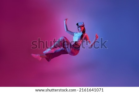 Amazed young woman using a virtual reality headset playing video games trying to touch something with hand floating in mid-air.