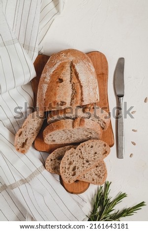 Fresh sliced rye bread on a wooden board, knife and rosemary on a white background. Top view.