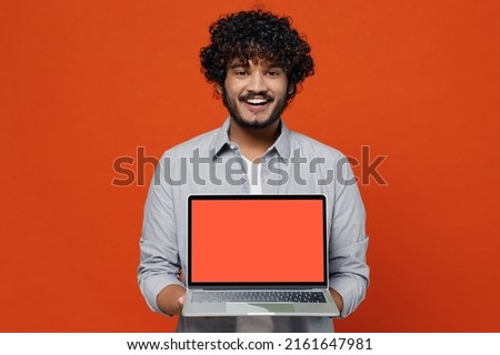Fascinating charismatic young bearded Indian man 20s years old wears blue shirt hold use work on laptop pc computer with blank screen workspace area isolated on plain orange background studio portrait Royalty-Free Stock Photo #2161647981