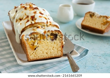 Piece of pound cake with fruit, cream icing and caramel served on a plate with a spatula on a blue textured background. Coffee break concept