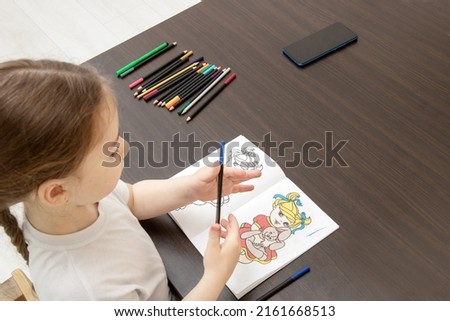 little girl with a pigtail sitting at the table chooses pencils for coloring according to the model.